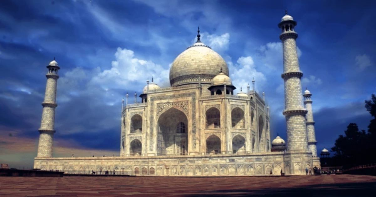 A wide-angle view of the Taj Mahal under a dramatic blue sky, highlighting the glowing marble dome and minarets during a Taj Mahal Night Tour.